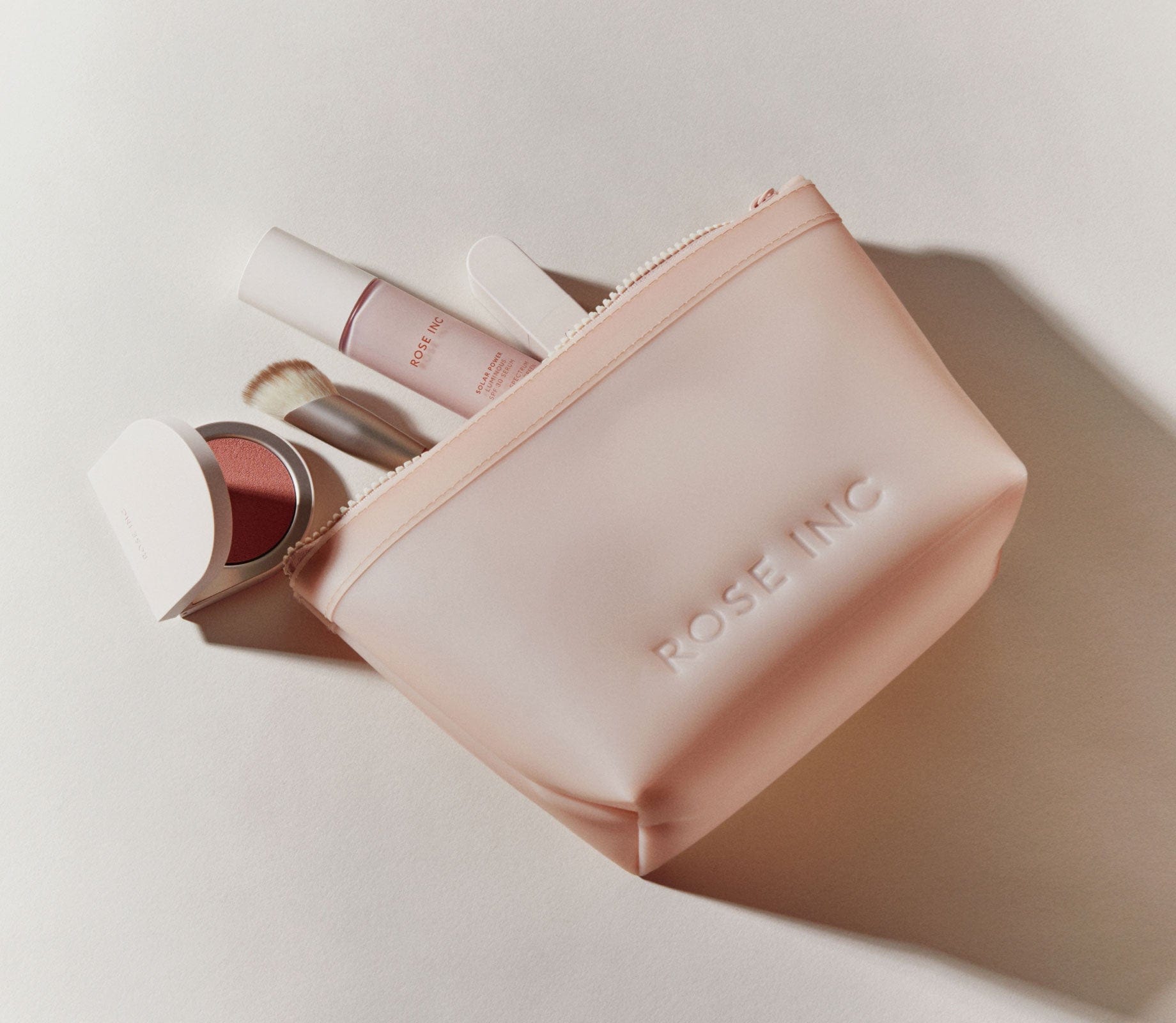 Photo of the Rose Inc Translucent Makeup Bag with signature products spilling out